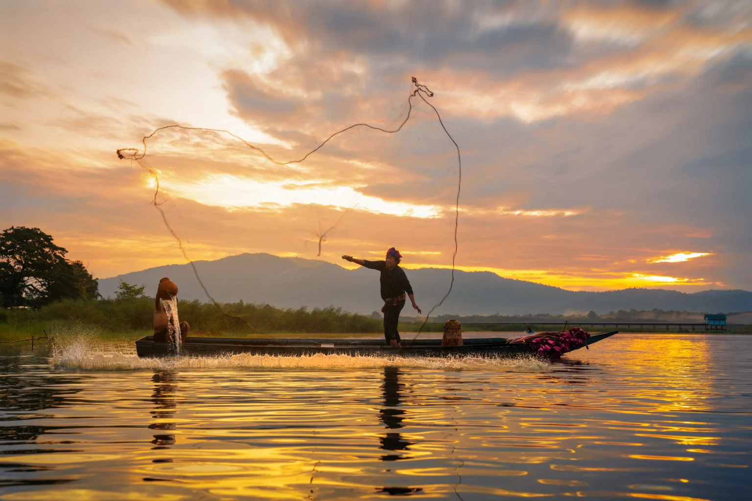 Angler, der bei Sonnenuntergang ein Netz von einem Boot auswirft
