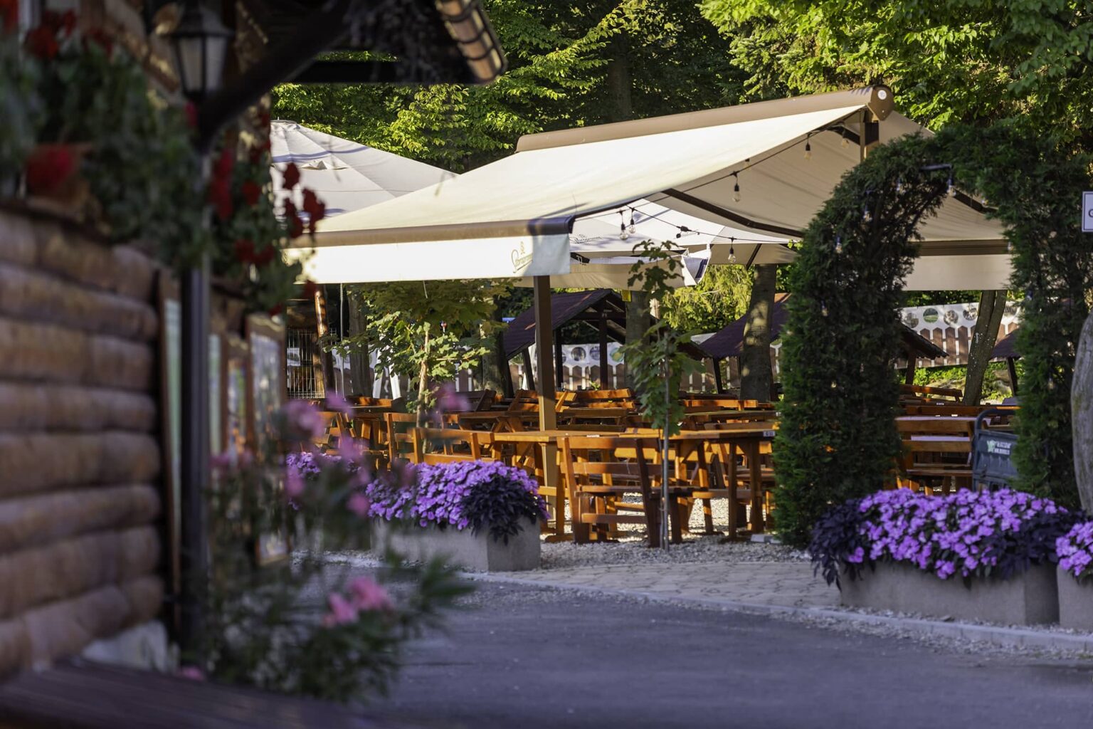 Der Sommergarten bei Sonnenuntergang, mit Blumen und Holztischen unter den Bäumen