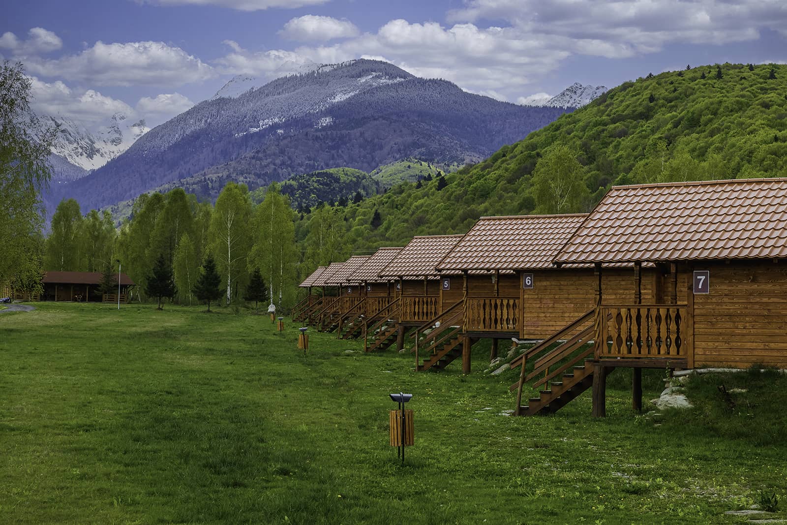 A row of numbered wooden cabins, with the Făgăraș Mountains behind