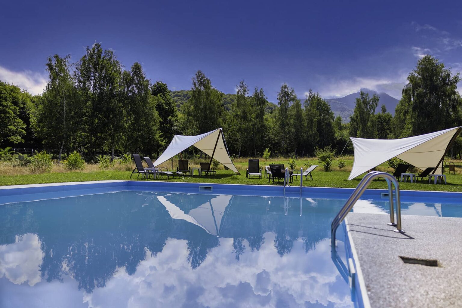 Der Außenpool im Sommer, mit Sonnensegeln und Liegen auf dem Rasen