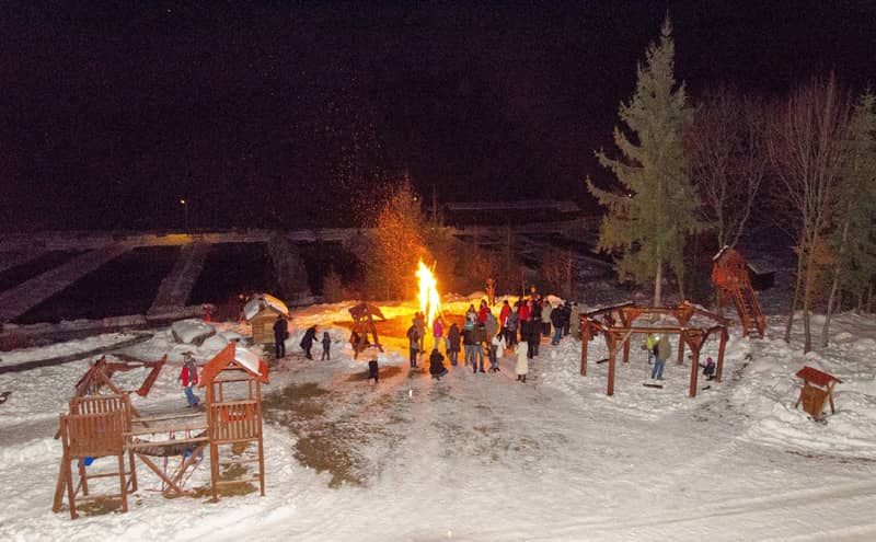 Lagerfeuer im Schnee am Abend, mit Holzbänken ringsum
