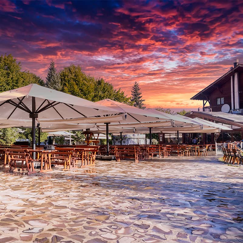 Terasa restaurantului la apus, cu umbrele mari și cerul roșiatic