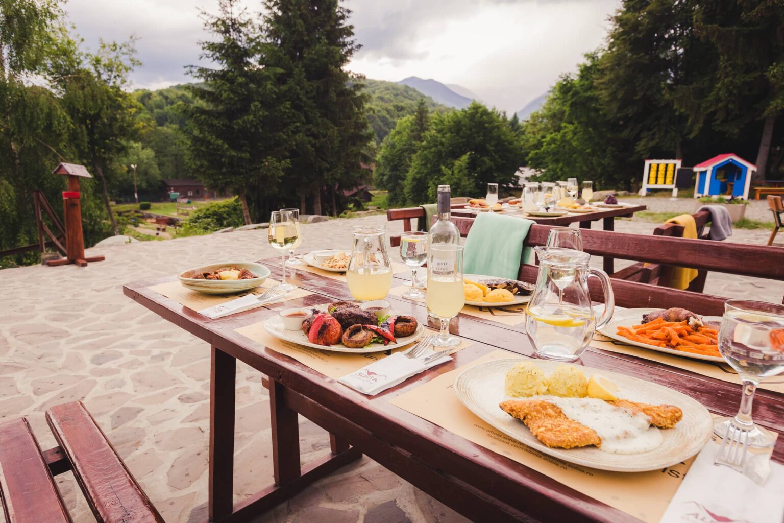 Masă pe terasă, cu file de păstrăv pane, platou de grătar, vin și limonadă