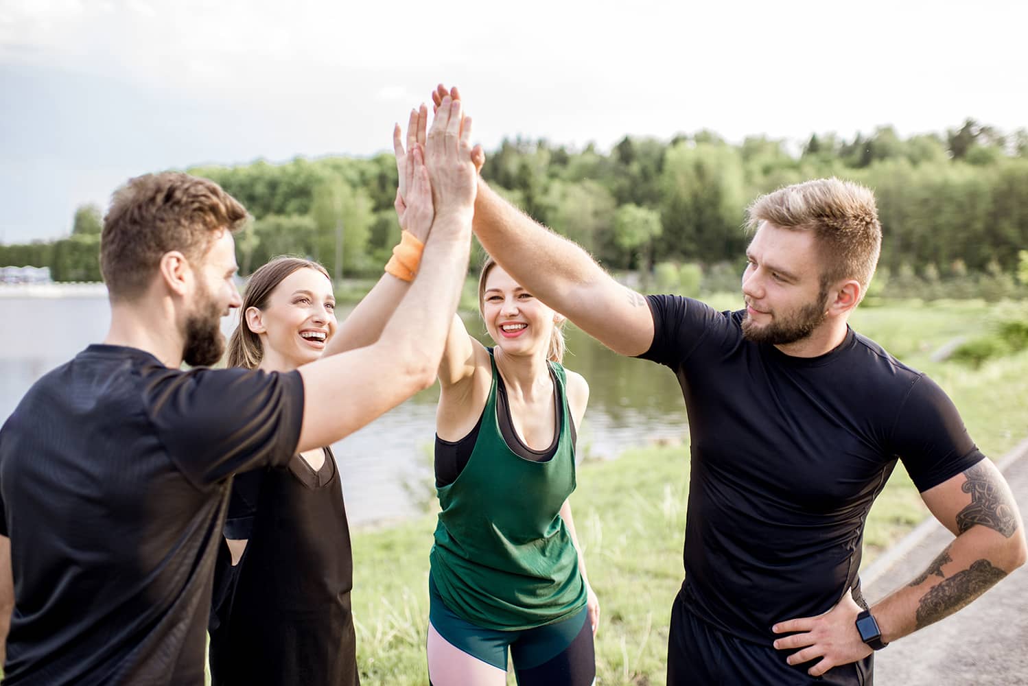 Four people in sportswear high-fiving beside a lake