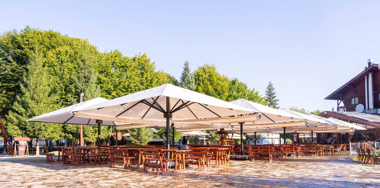 Die Sommerterrasse des Restaurants mit großen Sonnenschirmen und Holztischen