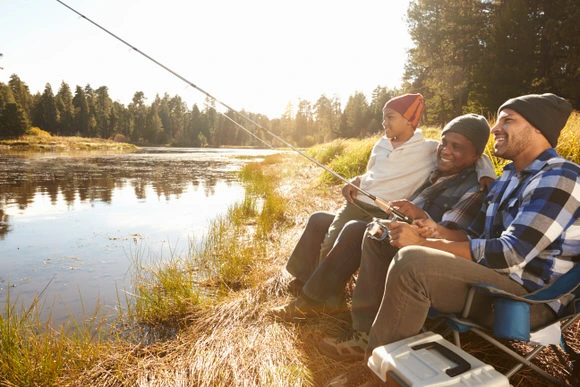 Three friends fishing on a river bank in the light of the sunset