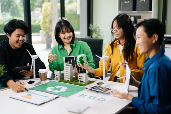 Vier junge Leute an einem Arbeitstisch mit dem Modell einer Windkraftanlage und Solarmodulen