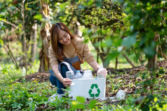 Frau sammelt Plastikflaschen in einem Recyclingkorb im Wald