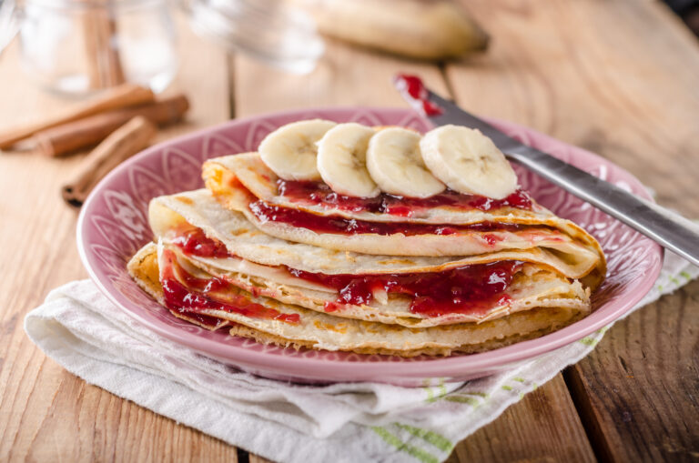 Pfannkuchen mit Konfitüre und Bananenscheiben auf einem rosa Teller