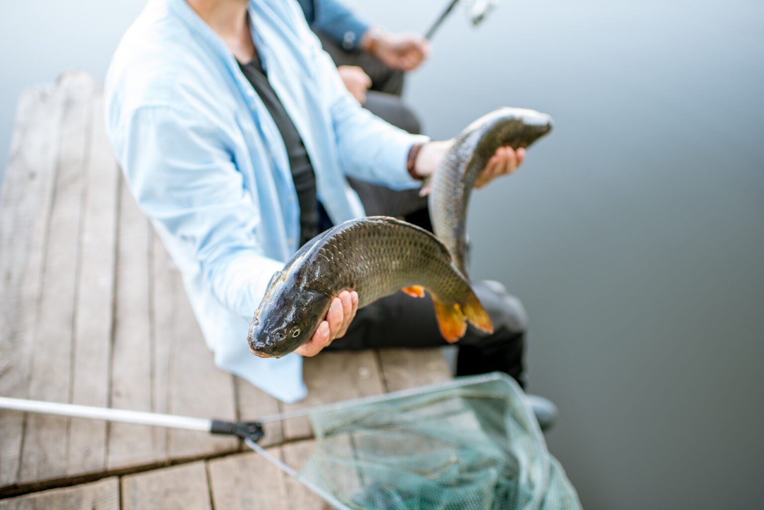 Angler auf dem Steg, mit zwei gefangenen Fischen