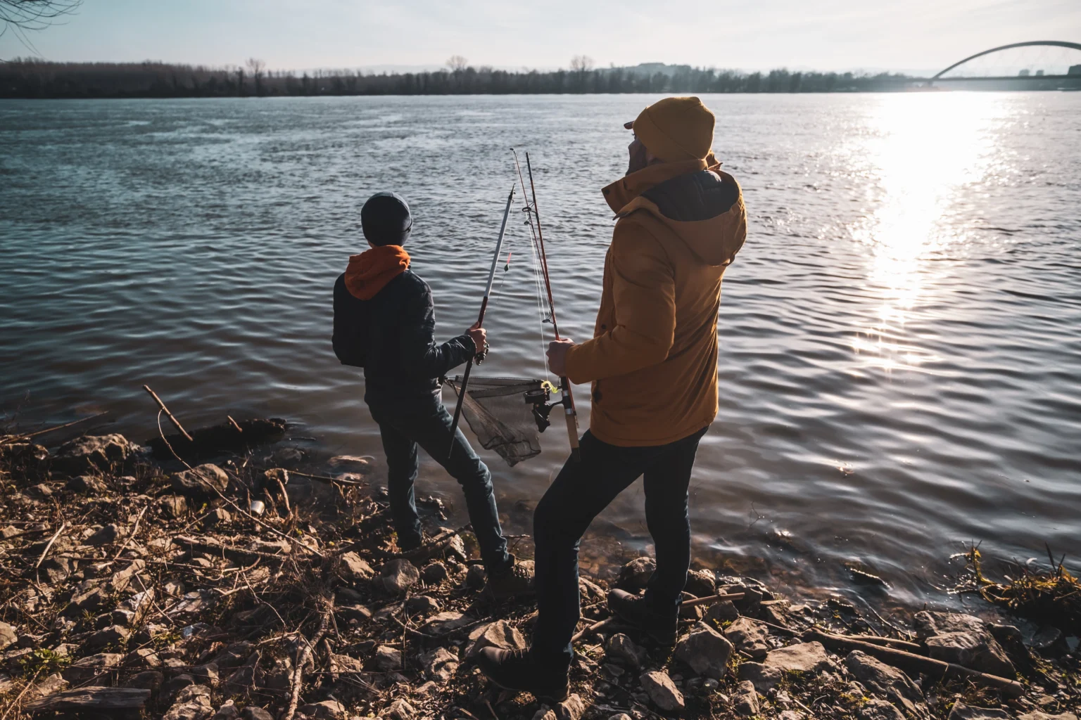 Two anglers on the stony bank of the river, in winter light
