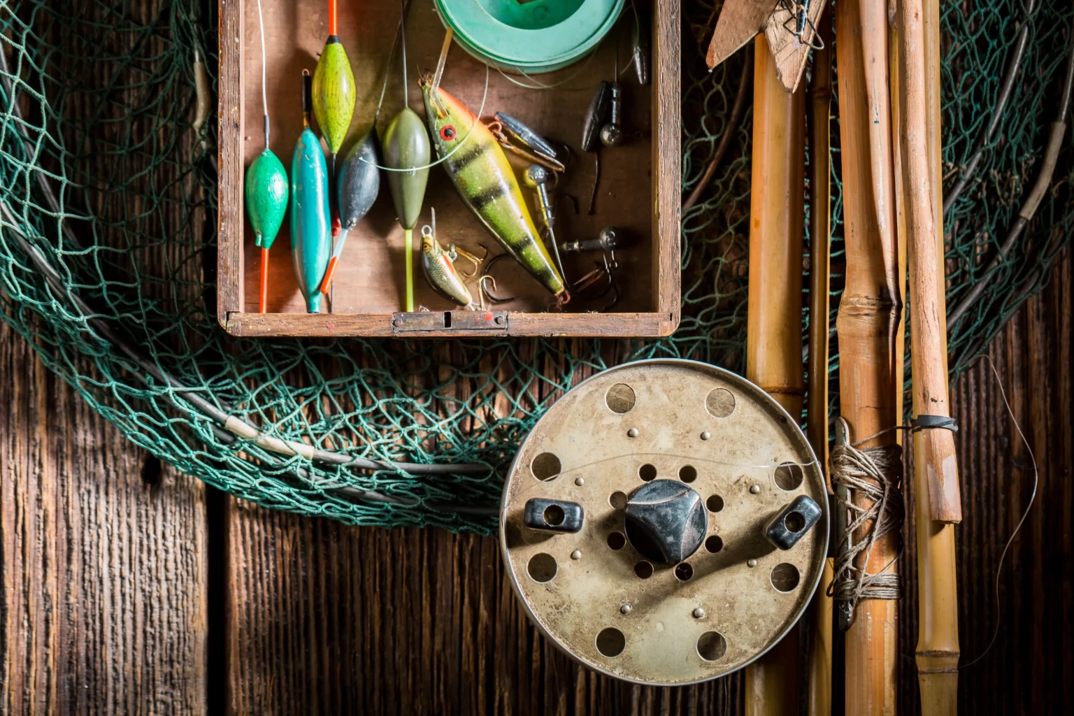 A box of floats and lures, a reel and bamboo rods, on a wooden table