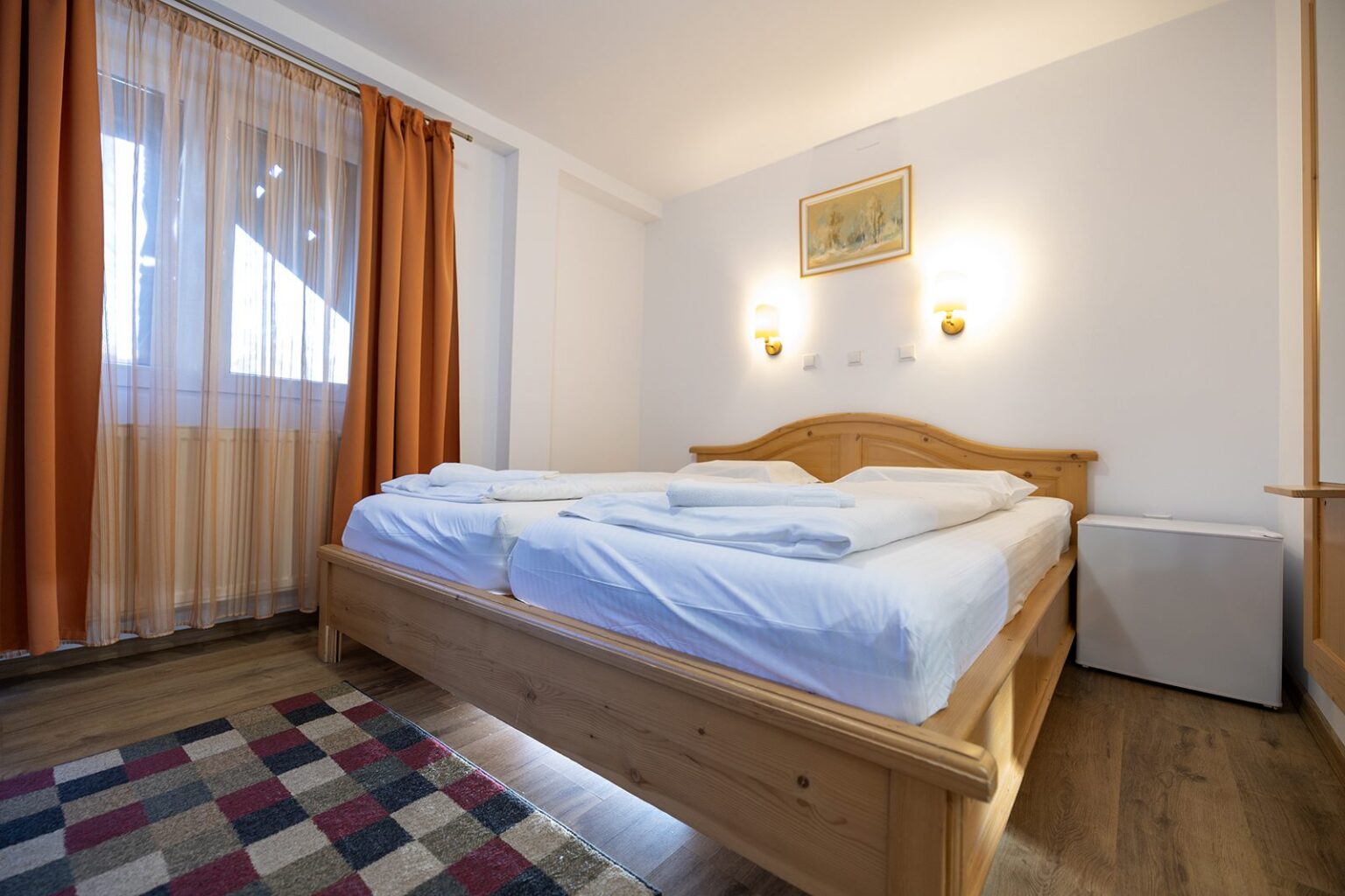 Hütte C: Schlafzimmer mit Doppelbett aus Holz und Fenster mit Vorhängen