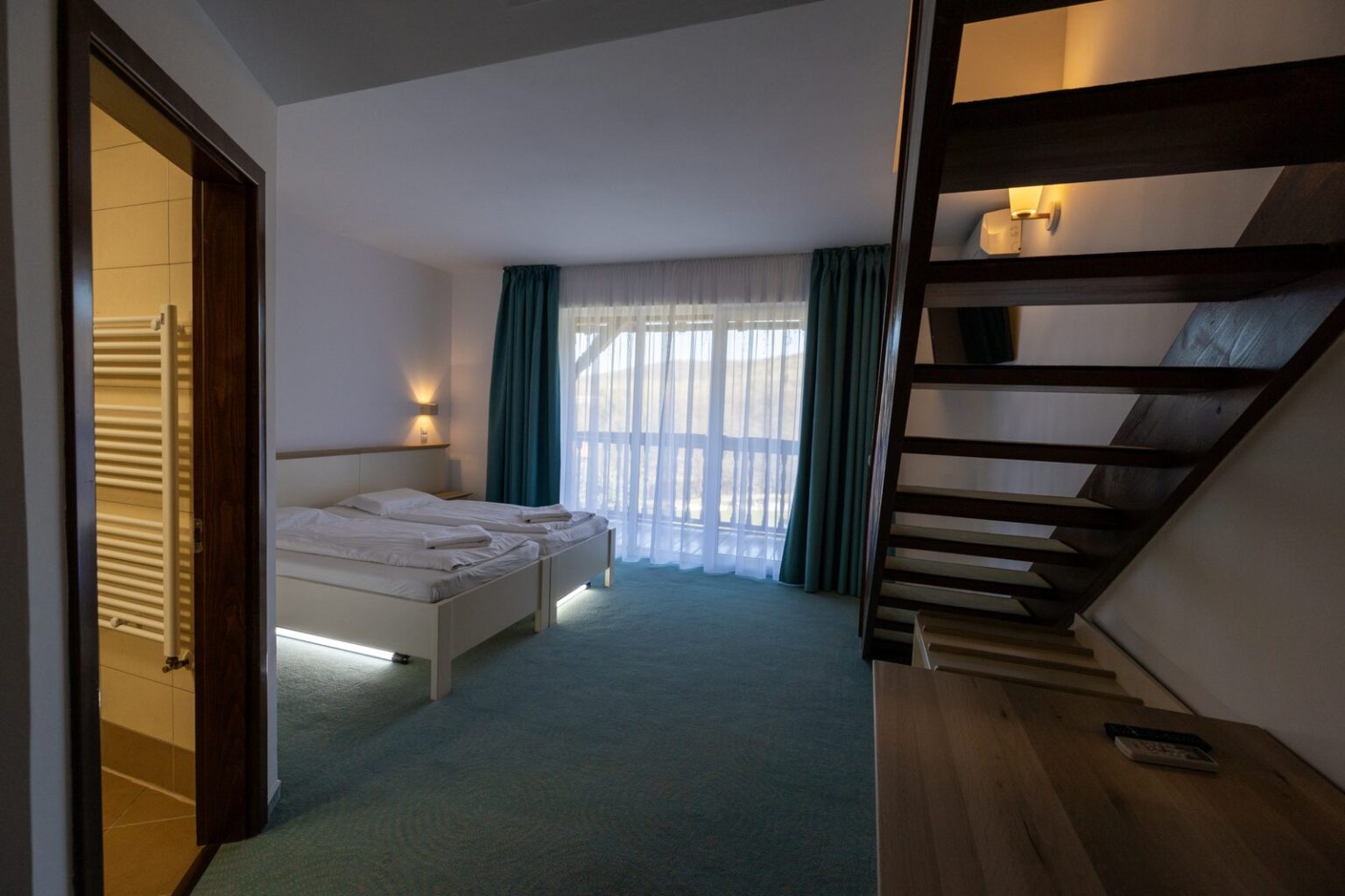 Junior Suite: dormitorul de jos, cu scara din lemn spre mansardă și ușa băii
