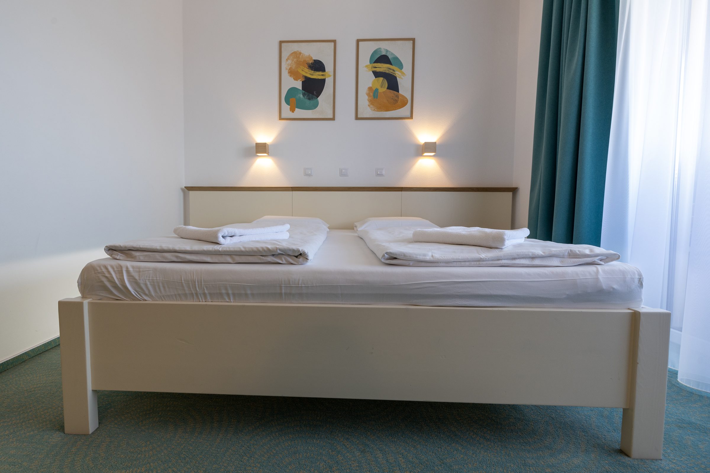 Double room: the double bed with wall lamps and teal curtains